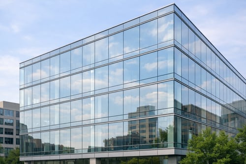 Oblique view of a mid‑rise building with glass curtain wall where the bird‑friendly dot pattern is barely noticeable at normal viewing distance, maintaining a clean, high‑performance façade.